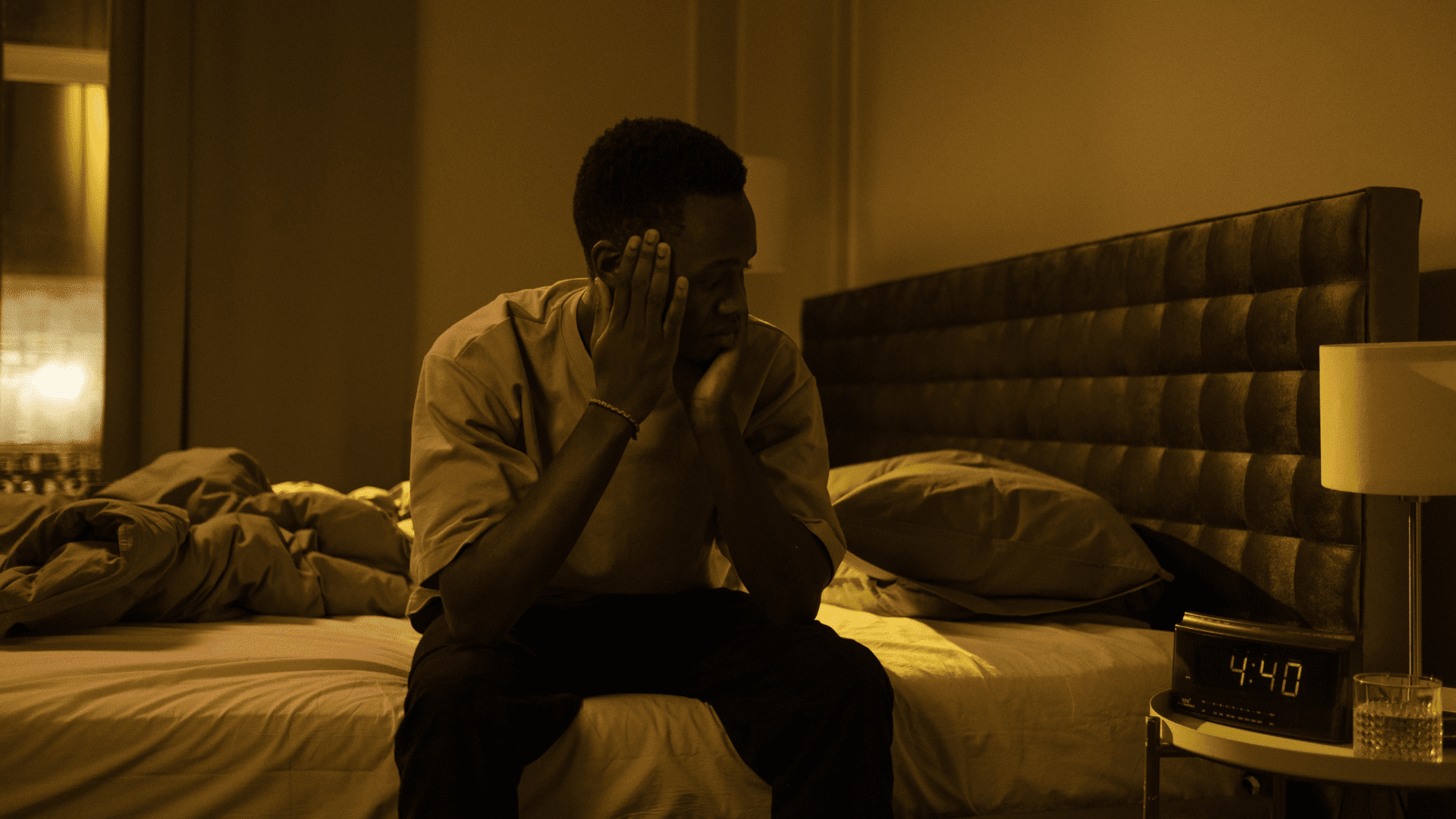 Man sitting on bed looking at alarm clock 4am