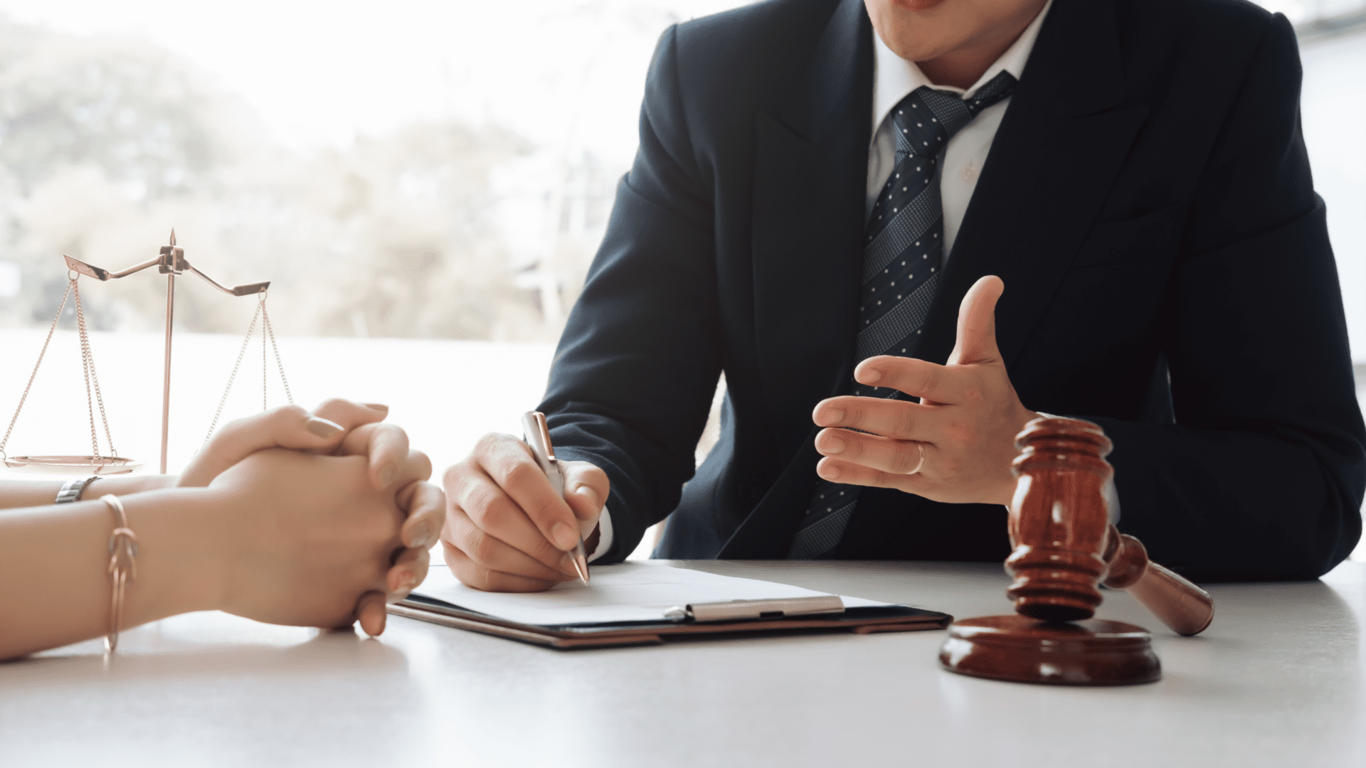 Man in suit sitting opposite a woman, he is writing on a clip board in front of a gavel 
