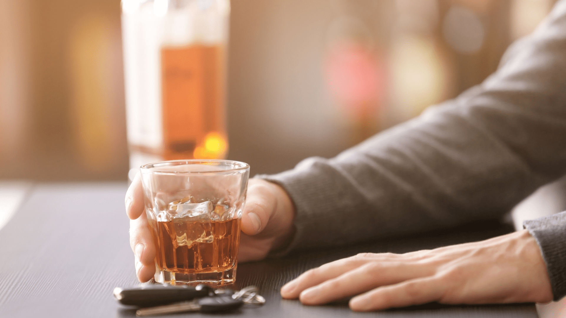 Person at bar with a glass filled with brown liquid and car keys next to them