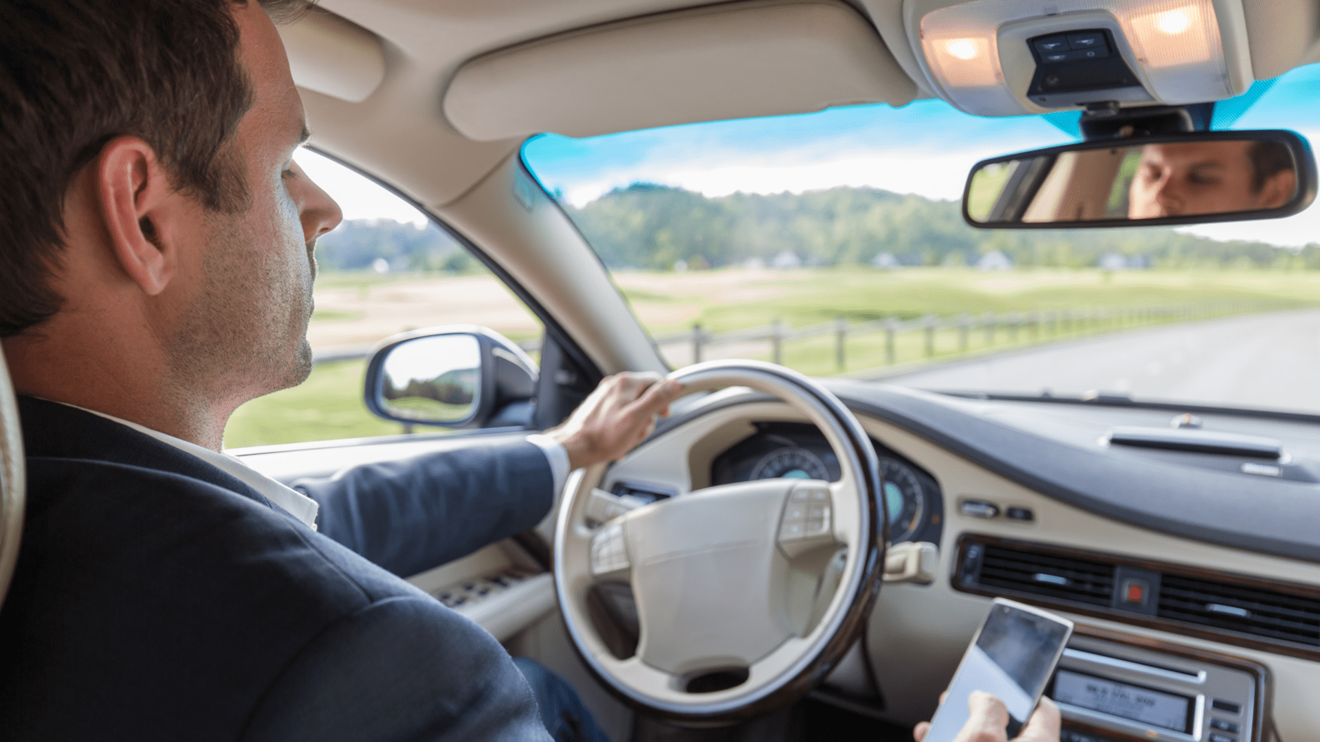 Man in suit sitting in car, holding phone in right hand and left hand on the wheel